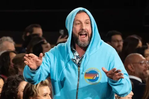 Adam Sandler in a blue hoodie at the Oscars, surrounded by audience members.