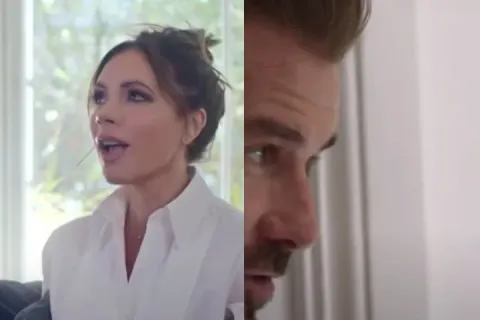 Victoria Beckham is sitting on a couch arguing with David Beckham peeking from behind a wall.