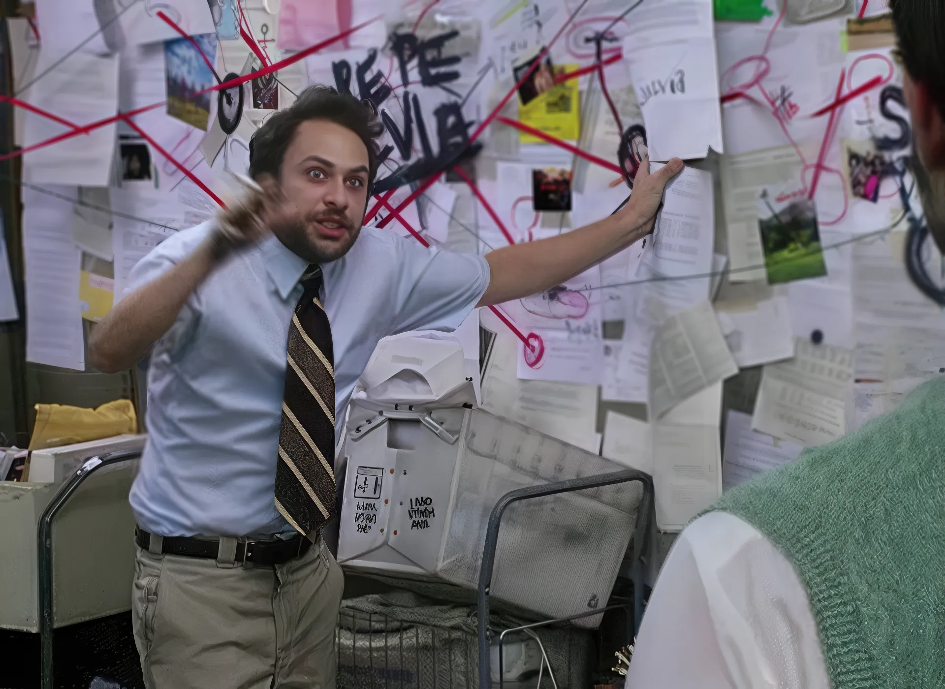 Charlie from It's always Sunny in Philadelphia in the office pointing at a chaotic wall of papers and red strings.