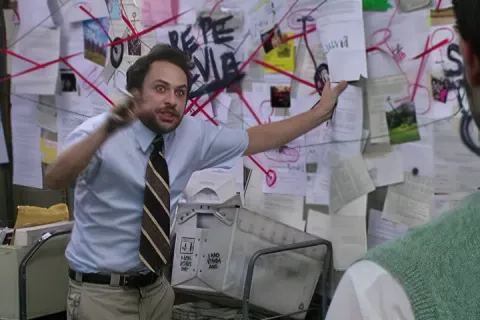 Charlie from It's always Sunny in Philadelphia in the office pointing at a chaotic wall of papers and red strings.