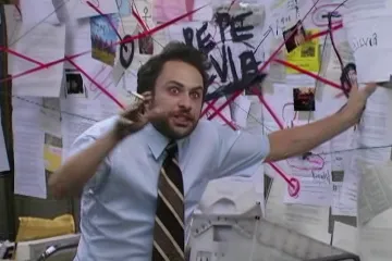 Charlie from It's always Sunny in Philadelphia in the office pointing at a chaotic wall of papers and red strings.