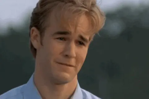 A young man with blonde hair crying, wearing a light blue shirt, outdoors.