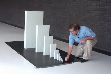 A man setting up a series of increasingly larger dominoes on a black surface.
