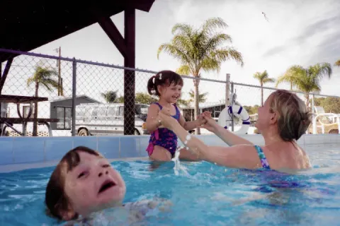A mother holding a child in a pool while another child struggles in the water.