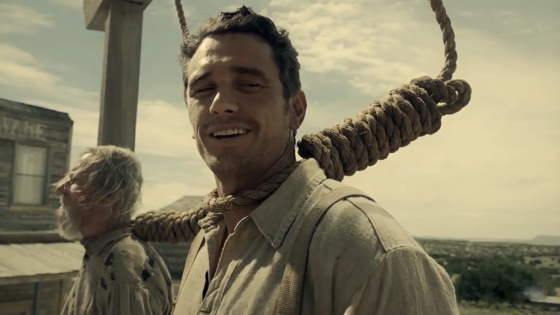A man with a noose around his neck smiling, from a movie scene.