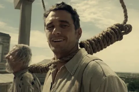 A man with a noose around his neck smiling, from a movie scene.