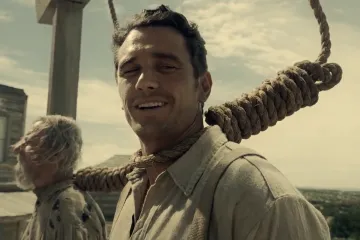A man with a noose around his neck smiling, from a movie scene.