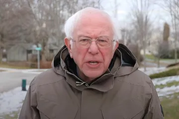 Bernie Sanders in a winter coat speaking outdoors with a serious expression.