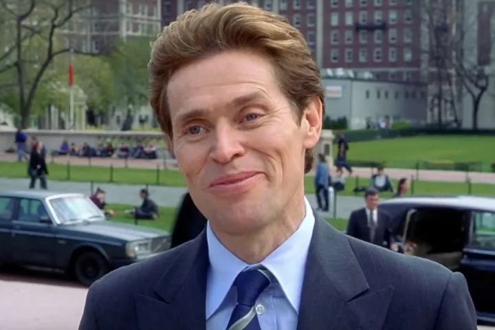 A man in a suit smirking outdoors, from a movie scene.