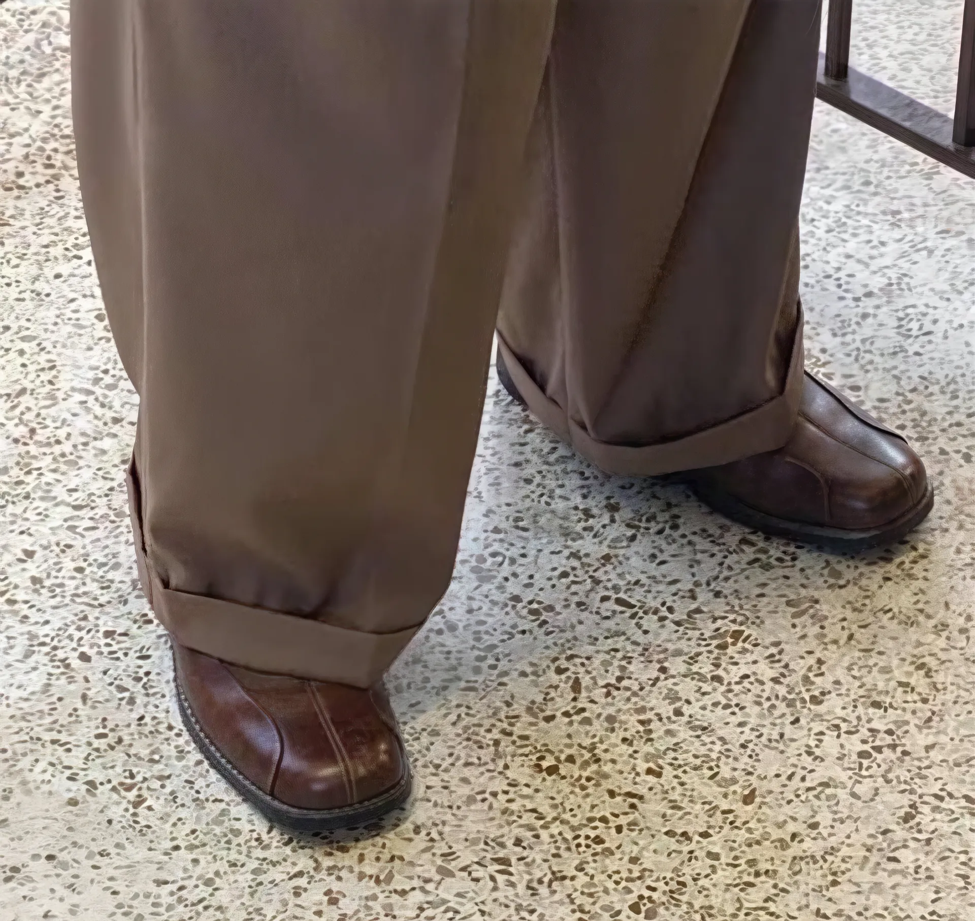 Close-up of oversized brown pants and shoes on a tiled floor.