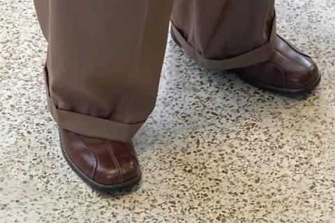 Close-up of oversized brown pants and shoes on a tiled floor.