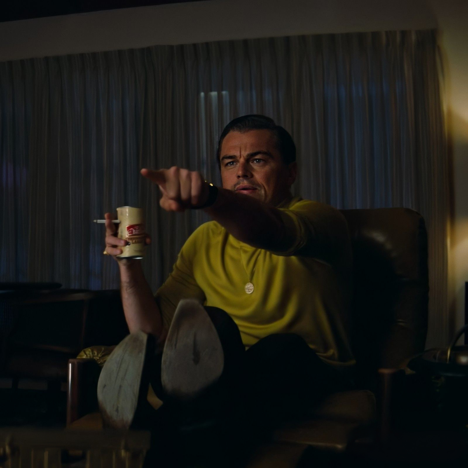 Leonardo DiCaprio pointing while holding a drink and cigarette in a movie scene.