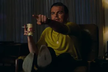 Leonardo DiCaprio pointing while holding a drink and cigarette in a movie scene.