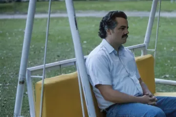 A man sitting on a swing, at a table, and by an empty pool, looking contemplative.