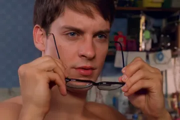 Peter Parker putting on glasses, a scene from Spider-Man.