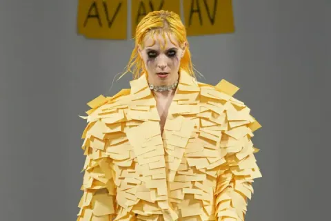 Model wearing a yellow Post-it note dress on a runway.
