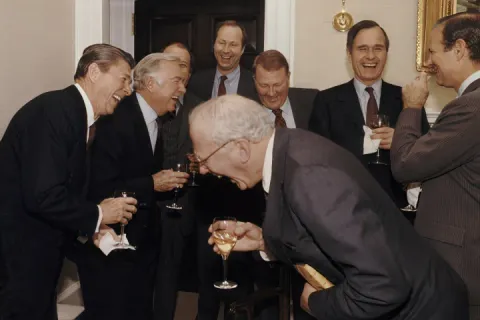 Group of men in suits laughing and holding drinks in a formal setting.