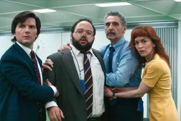 A man in a white turtleneck looks serious. Four people in office attire appear frightened.