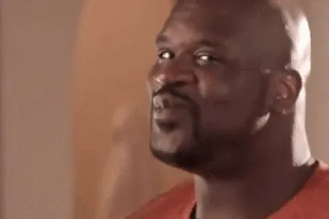 A person in an orange shirt playfully shaking their shoulders and smiling.