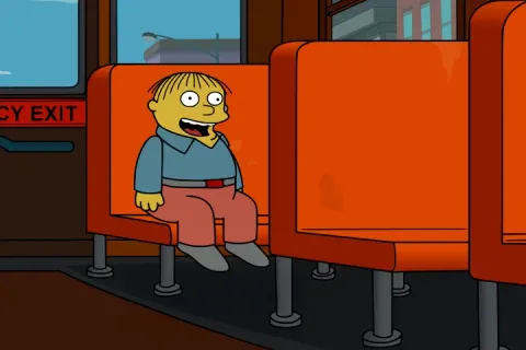 Ralph Wiggum sitting on a school bus with an emergency exit sign behind him.