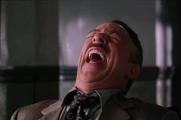 A man in a suit laughing heartily in an office setting.