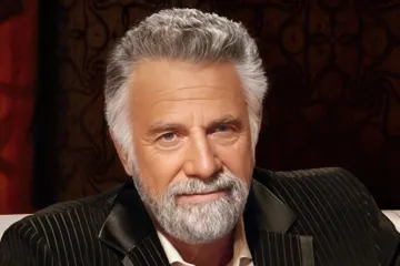 A distinguished man with a beard sitting at a table with a beer bottle.