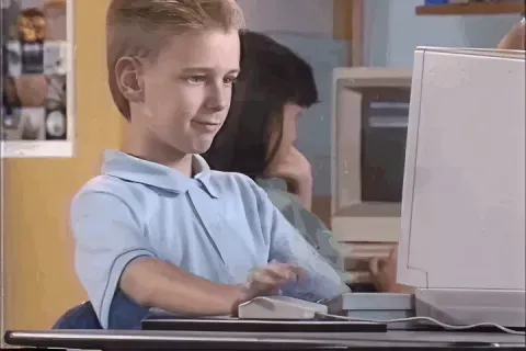 Young boy giving a thumbs up while using a computer.