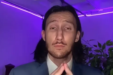 Person in a suit with hands clasped, purple lighting in the background.