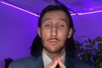 Person in a suit with hands clasped, purple lighting in the background.