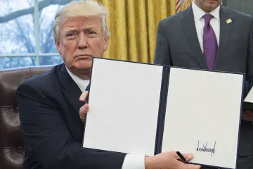 Donald Trump holding a signed blank document in the Oval Office.