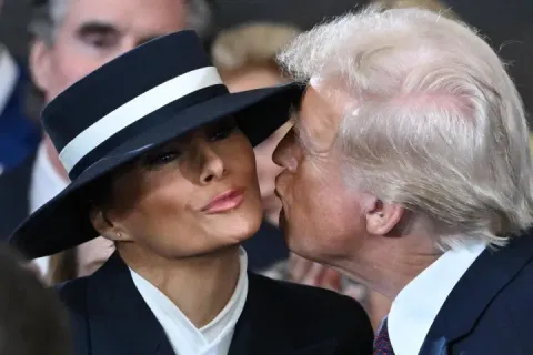 Donald Trump kisses Melania Trump, who is wearing a wide-brimmed hat.