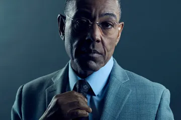 A serious man in glasses adjusting his tie in a dark suit.
